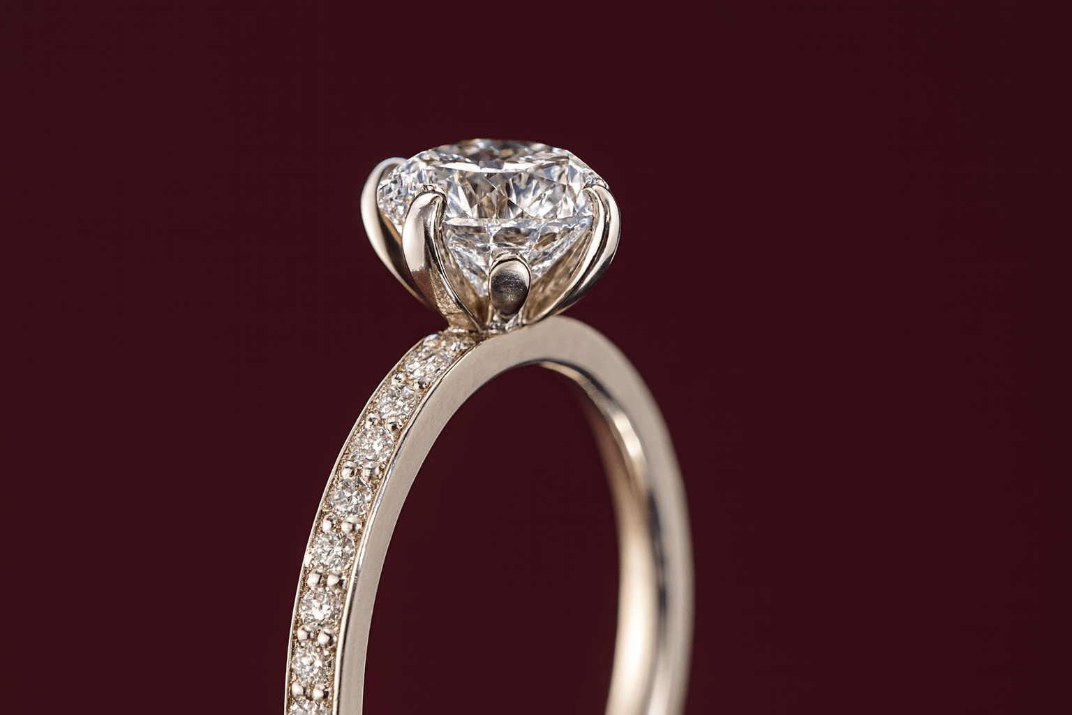 A close up of a diamond ring in white gold with petal-like claws, with a maroon background
