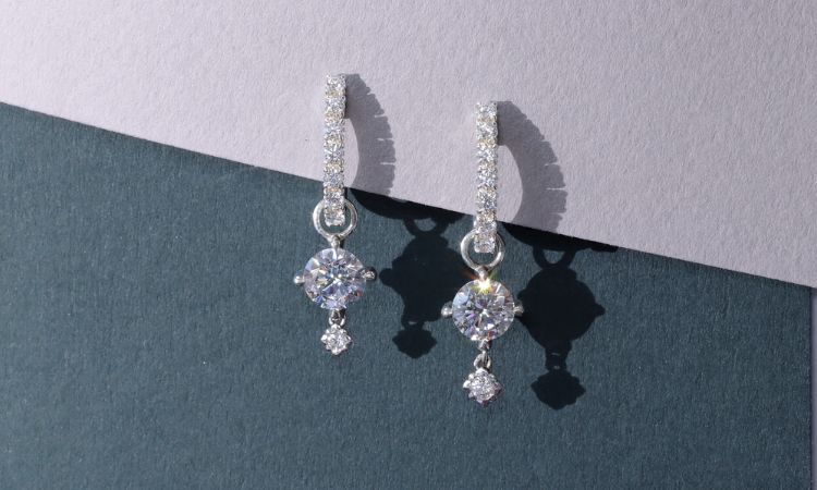 Pair of diamond earrings with diamond hoops on a gray and blue background