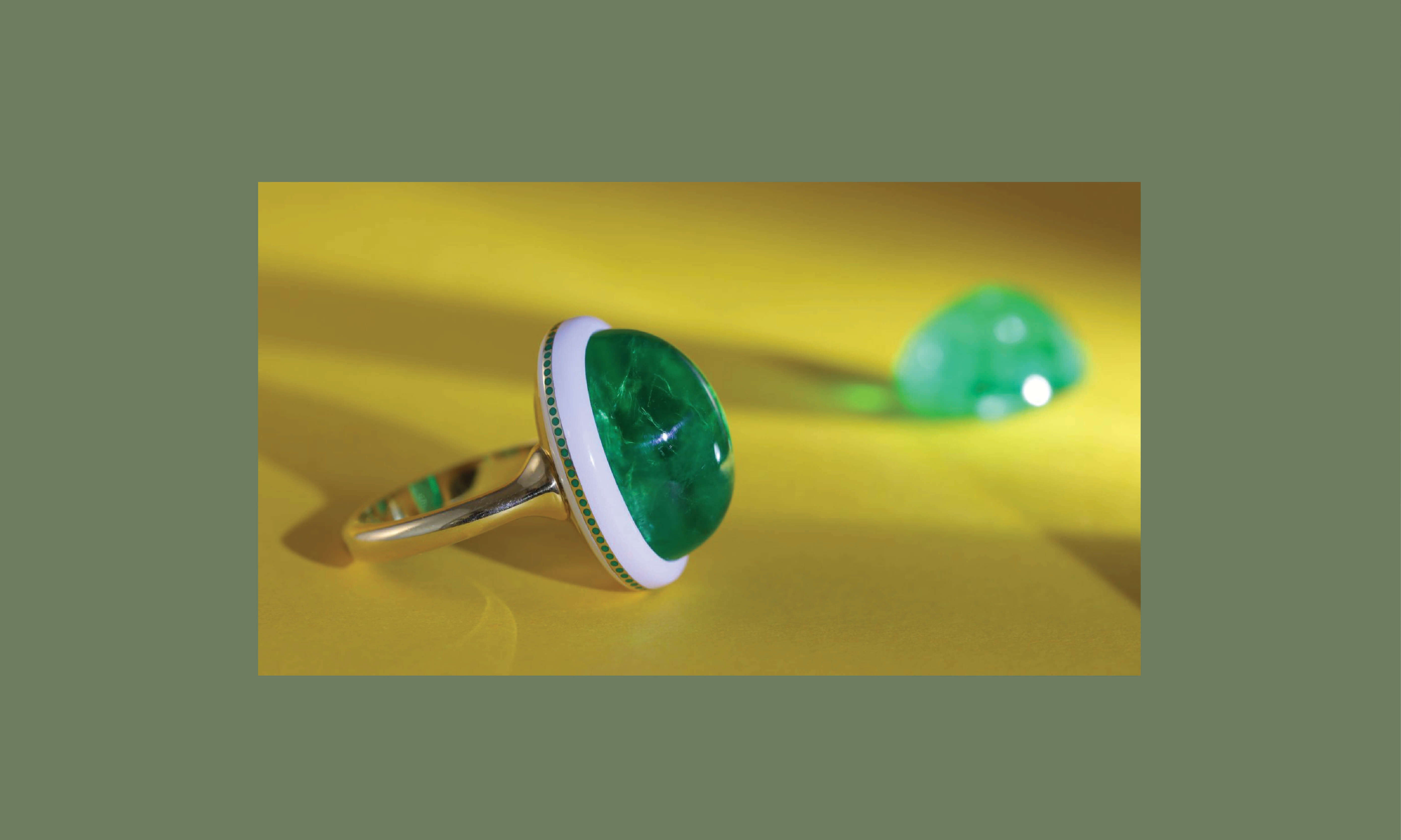 Emerald ring with enamel detail, in front of a loose, fine gemstone